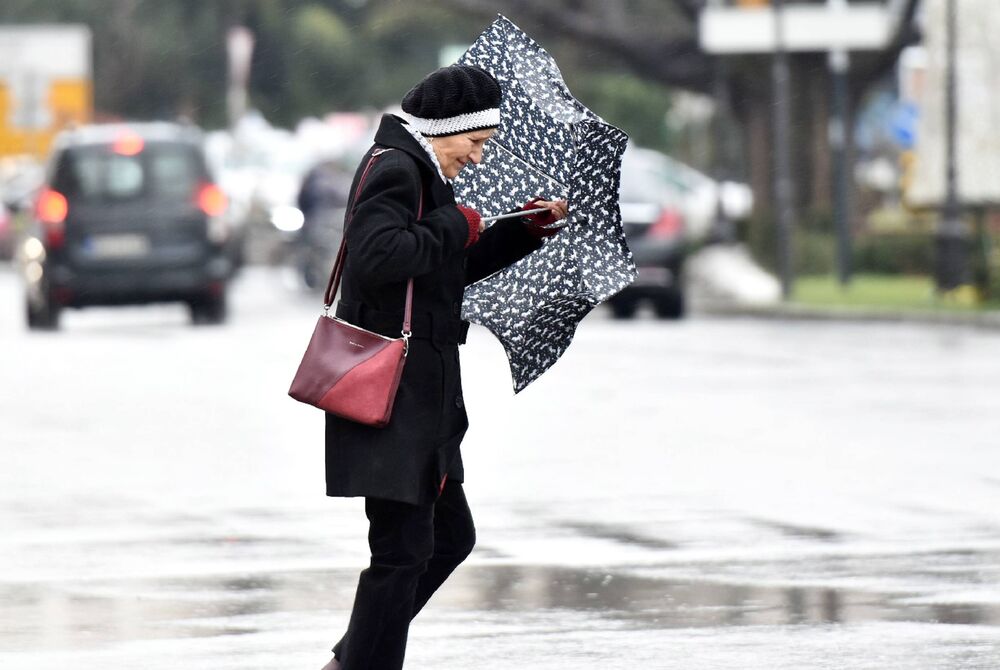 Žea stoji i drži kišobran da ne odleti